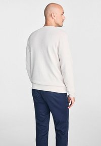 Jasno beżowy sweter o prążkowanej fakturze, okrągłym dekolcie i dopasowanym wykończeniu, w połączeniu z ciemnoniebieskimi spodniami z tylnymi kieszeniami.