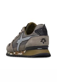 Zapatilla con parte superior de ante en color marrón claro, acentos en gris oscuro, logo plateado, suela con patrón de camuflaje y un parche trasero negro con detalle del logo.
