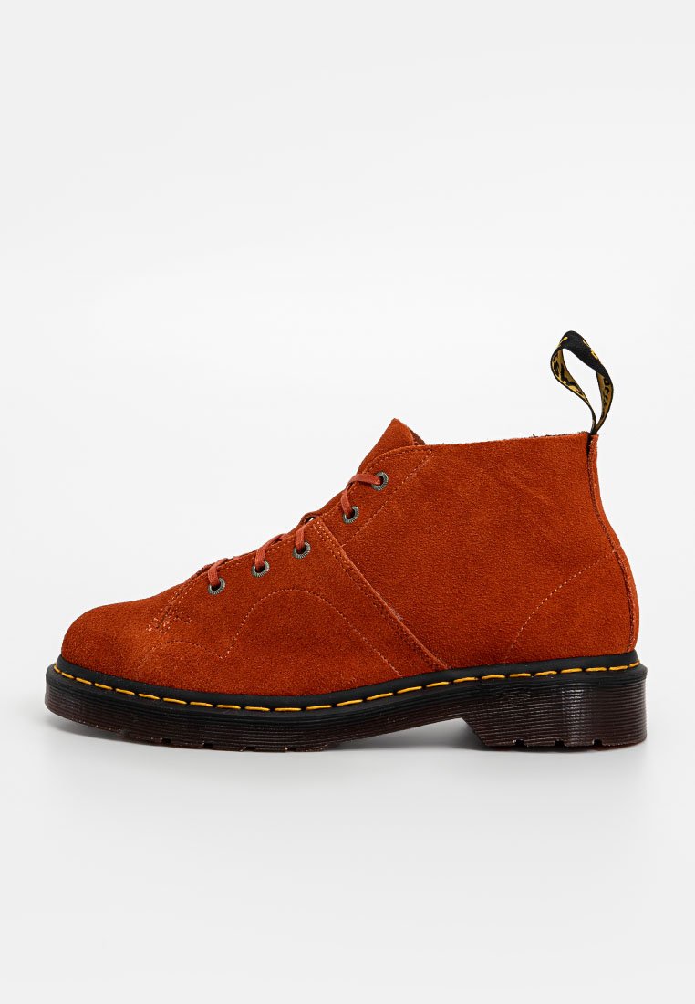 Rustfarbene Wildleder-Ankle-Boots mit schwarzer Sohle, gelben Nähten, Schnürung vorne und einem Zugband an der Rückseite.