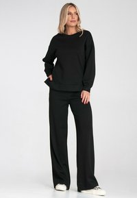 Czarny sweter i szerokie spodnie z miękkiego materiału. Posiada luźny krój, okrągły dekolt i przednie kieszenie. W zestawie z białymi sneakersami.