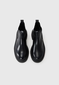 Botas de tobillo de cuero negro con una superficie lisa, puntera redondeada, paneles laterales elásticos y una suela negra gruesa. Sin herrajes o acentos visibles.