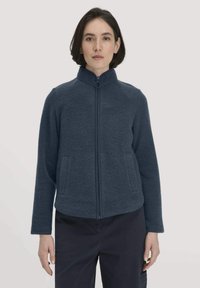 Marineblauwe fleecejas met een hoge kraag, een ritssluiting aan de voorkant en zijzakken. Heeft een zachte textuur en een comfortabele pasvorm.