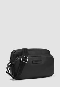 Borsa a tracolla in pelle nera con due scomparti, finitura strutturata, tracolla regolabile e dettagli in metallo argentato. Etichetta del marchio visibile.