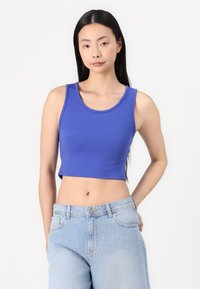 Gekürztes blaues Tanktop aus geripptem Stoff, mit Rundhalsausschnitt und breiten Trägern, kombiniert mit hellblauen hoch taillierten Jeans.
