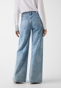 Hele sinised laiapõhjalised teksad, mis on valmistatud denimist, kõrge vöökohaga, kahe tagataskuga ja peenete tuhmuvate lillemustritega.