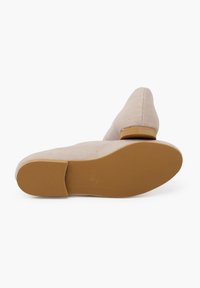 Beige Stoff-Slipper mit runder Zehenbox und einer niedrigen, flexiblen braunen Gummisohle. Die Oberfläche ist glatt mit einem dezenten Webmuster.