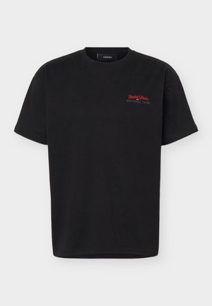 T-shirt noir à manches courtes avec petit texte rouge et blanc « United States National Team » sur la partie supérieure gauche de la poitrine.