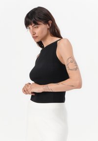 Zwarte geribbelde tanktop met een hoge hals en één schouderband, gecombineerd met witte hoge taillebroeken. Glad materiaal en getailleerd ontwerp.