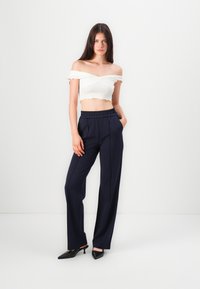 Hvit av-skulder crop-top med volangdetaljer, sammen med marineblå, høy midje, vide bukser. Sorte spisse hæler.