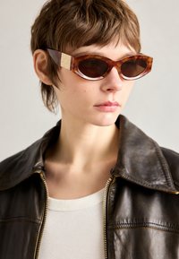 Cat-eye sunglasses with a tortoiseshell pattern and dark lenses, featuring golden hexagonal accents on the temples.