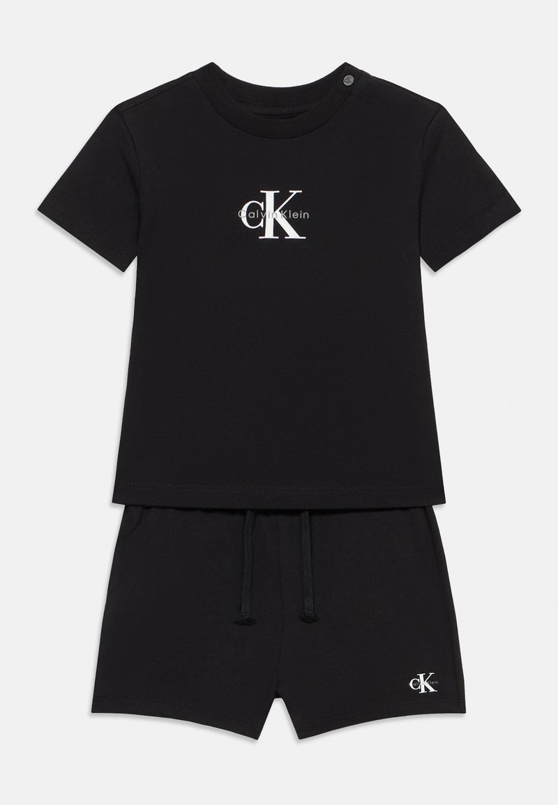 Σετ από κοντομάνικο μπλουζάκι και σορτς σε μέγεθος για νήπιο, μαύρου χρώματος, με λευκό λογότυπο Calvin Klein "cK" στο στήθος και στο τελείωμα των σορτς, με κουμπί στον ώμο του μπλουζάκι.