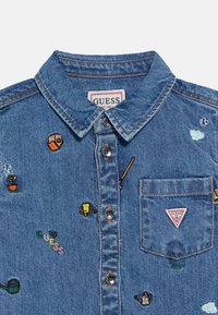 Τζιν πουκάμισο με γιακά, κουμπιά μπροστά και πολύχρωμα κεντημένα μοτίβα, όπως φυτά και εργαλεία. Διαθέτει τσέπη στο στήθος με λογότυπο.