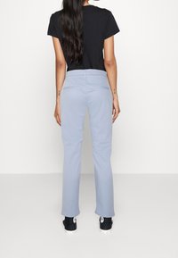 Jasnoniebieskie spodnie o prostym kroju z gładką fakturą i tylnymi kieszeniami. Połączone z czarną koszulką i czarnymi trampkami.