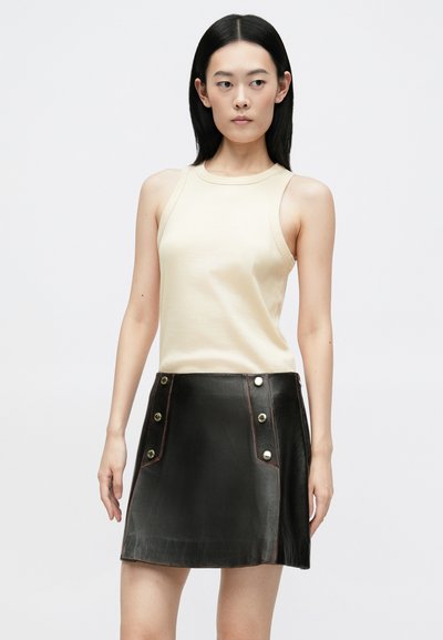 Bežs bez piedurknēm topiņš, apvienots ar melnu ādas mini svārku, kas rotāts ar zelta toņu pogām un kontrastējošu rozā diegu šuvēs.