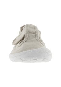 Zapato de lona beige claro con punta redonda, cinta de Velcro y suela de goma blanca texturizada. Detalles de costura a lo largo del empeine.