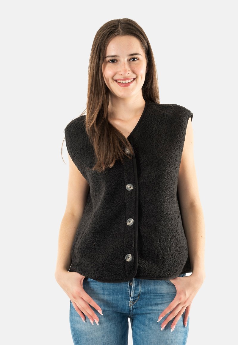 Chaleco de forro polar negro con una textura suave, diseño sin mangas, escote en forma de v y cinco botones plateados en el frente. Llevado sobre jeans azules.