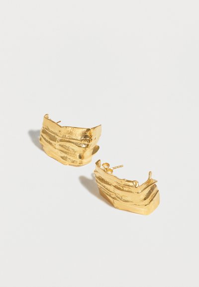 Ζευγάρι στρογγυλών σκουλαρικιών από χρυστό μέταλλο με υφή και ακανόνιστο, οριζόντιο αυλακωτό σχέδιο σε λευκό φόντο.