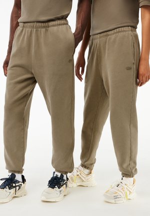 Dwie osoby w pasujących khaki dresach i trampkach, stojące obok siebie z rękami swobodnie opuszczonymi wzdłuż ciała.