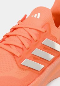 Πορτοκαλί αθλητικό παπούτσι με υφασμάτινο άνω μέρος με υφή, διακοσμημένο με κορδόνια με υφή και τρεις ασημένιες ρίγες στο πλάι. Ελαφρύς σχεδιασμός.