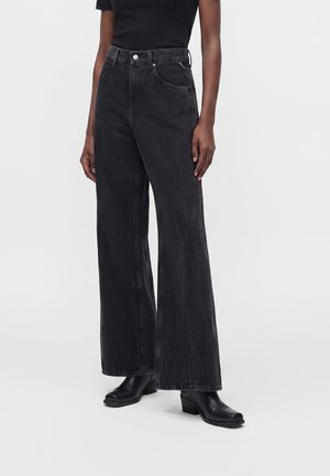 Person iført sorte vidde jeans med høj talje, kombineret med sorte ankelstøvler med hæl og en sort t-shirt med korte ærmer.