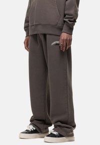 Graue, locker sitzende Sweatpants mit elastischem Bund, seitlichen Taschen und dezentem Branding am linken Oberschenkel. Hergestellt aus weichem Baumwollmaterial.