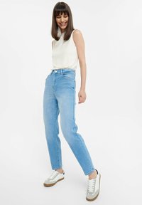 Jeans de tiro alto en un azul claro con un corte recto, combinados con una blusa sin mangas color crema y zapatillas blancas con detalles en gris.