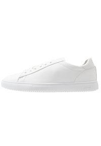 White leather sneaker with rounded toe, flat rubber sole, and minimal stitching. Features lace-up front and brand logo on the heel.