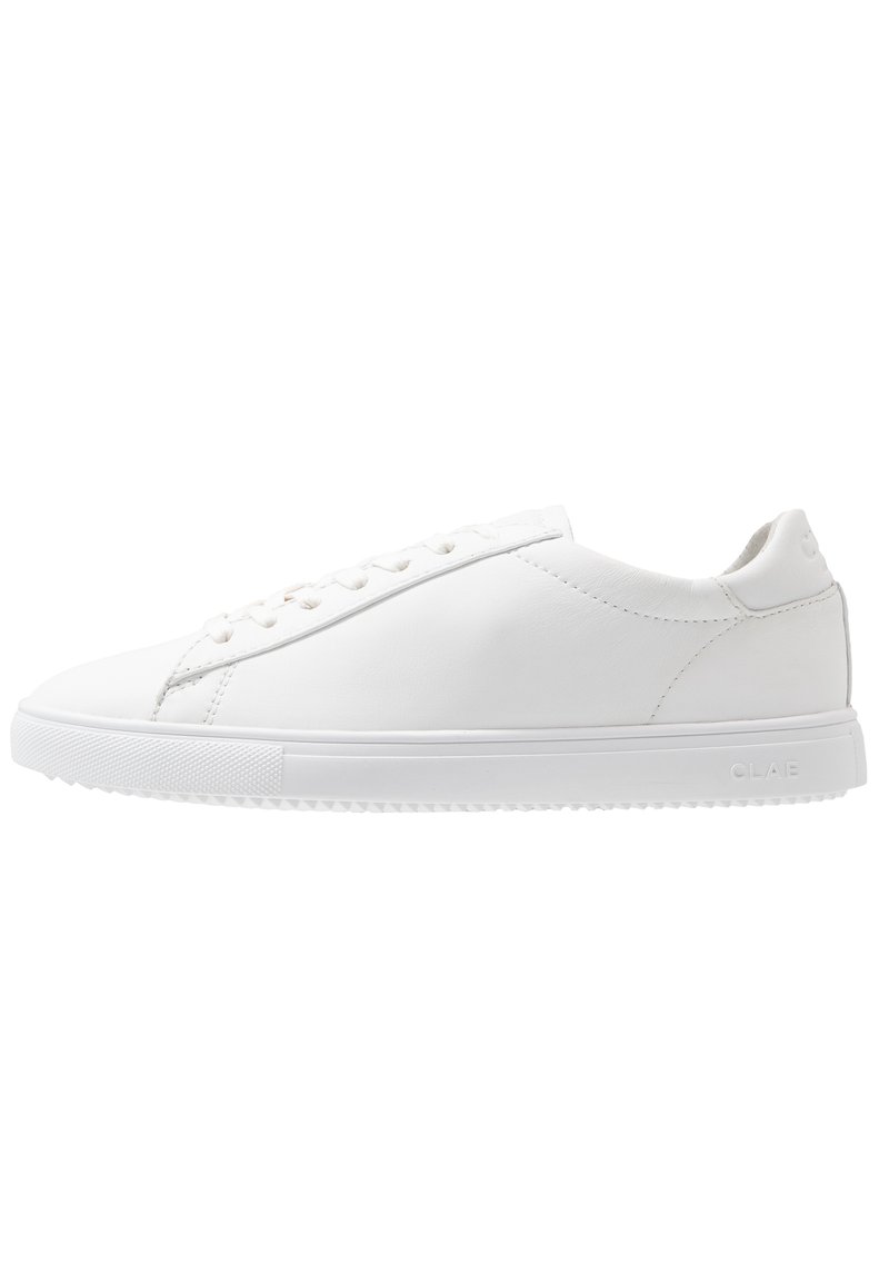 White leather sneaker with rounded toe, flat rubber sole, and minimal stitching. Features lace-up front and brand logo on the heel.