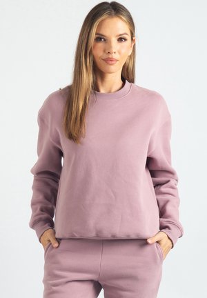 Liliowa bluza z miękkiego materiału, z długimi rękawami, prążkowanym, okrągłym dekoltem i luźnym krojem. Posiada boczne kieszenie użytkowe.