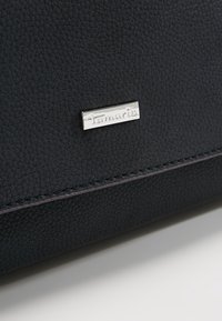 Marinblå läderhandväska med en texturerad yta, silverfärgad detalj med logotyp och kontrasterande sömmar längs kanterna.