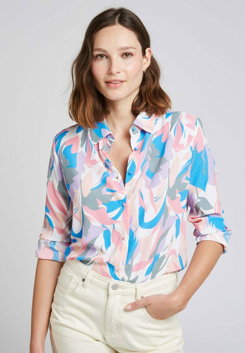 Chemise à boutons en tissu léger à motifs, présentant des formes abstraites rose, bleu et gris ; manches retroussées ; texture douce.