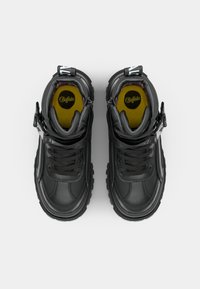 Black sneakers with textured leather, chunky soles, and distinct lacing. Inside features a yellow insole with a logo. Black and gray accents throughout.