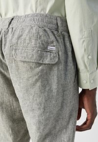 Pantalons en lin gris avec ceinture élastique, détails de poche arrière et petite étiquette. Associés à une chemise vert clair avec un motif subtil.