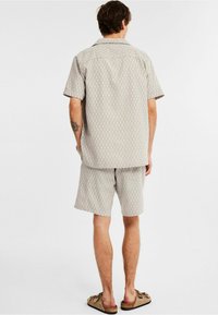 Ensemble de chemise à manches courtes et de shorts en beige clair avec un motif en losanges. Fabriqué en tissu doux ; coupe décontractée avec un col en V.