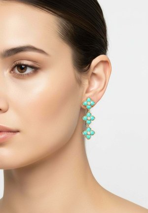 Primo piano di una donna che indossa orecchini d'oro con tre grappoli di trifogli turchesi appesi verticalmente.