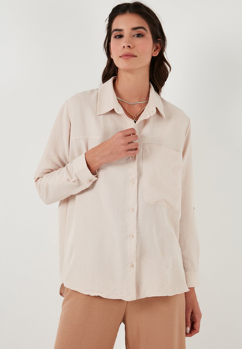 Lichtbeige, lange mouwen shirt met kraag, knoopsluiting aan de voorkant en een borstzak. Zachte textuur, relaxte pasvorm, gecombineerd met bijpassende beige broek.