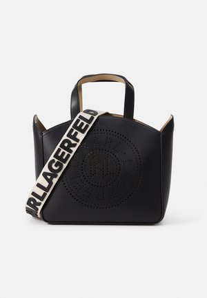 Sac cabas noir avec logo circulaire perforé et large sangle crème avec texte noir gras « KARL LAGERFELD ».