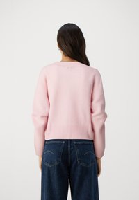 Rosa gerippter Pullover mit rundem Ausschnitt und halblangen Ärmeln, kombiniert mit dunkelblauen Jeans mit weitem Bein. Die Rückansicht hebt Textur und Passform hervor.