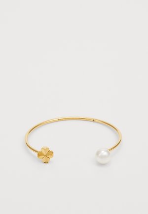 Gold metal cuff bracelet with a floral detail on one end and a round white pearl on the other. The design is sleek and minimalistic.