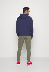 Dunkelblaue Kapuze mit einer entspannten Passform. Kombiniert mit olivgrünen Jogginghosen und roten Turnschuhen. Einfaches Design, einfarbige Farben.