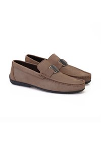 Braune Wildleder-Slipper mit flacher Gummisohle, die mit einem dekorativen Metallelement und steppdetail am oberen Teil ausgestattet sind.