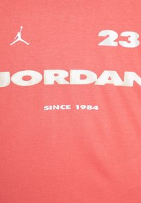 Camiseta de algodón en color coral con gran texto blanco que dice "JORDAN", "23" arriba y "SINCE 1984" abajo, con un logo de Jumpman en blanco.