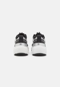 Schwarz-weiße Sportschuhe mit einer klobigen Sohle, reflektierenden Akzenten und gestreiften Mesh-Details an der Ferse und den Seiten.