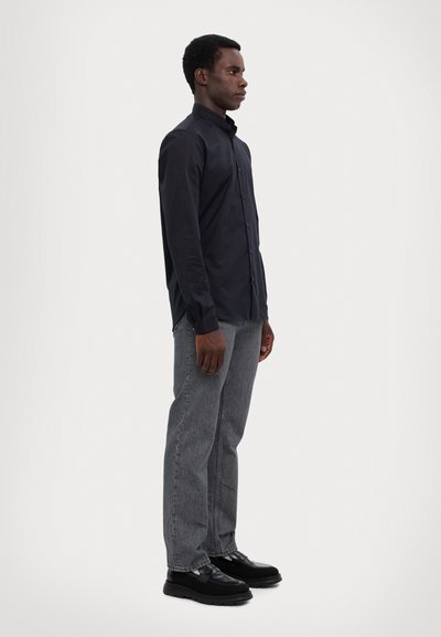 Marineblaues Hemd mit Kragen, graue Denim-Jeans und schwarze Schuhe. Das Hemd hat eine glatte Textur; die Jeans sind leicht locker geschnitten.