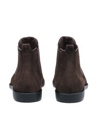 Brązowe zamszowe botki za kostkę o gładkiej fakturze, zaokrąglonym kształcie oraz czarnych gumowych podeszwach. Posiadają minimalne przeszycia i pętelki do łatwego zakładania.