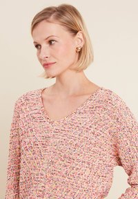 Mehrfarbiger strukturierter Pullover mit V-Ausschnitt. Der Stoff weist pinke, gelbe und blaue Fasern auf und zeigt ein gewebtes Muster.