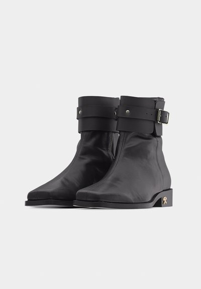 Ζευγάρι μαύρα δερμάτινα μποτάκια αστραγάλου με πλαϊνό φερμουάρ, φαρδιά τρύπα με αγκράφα γύρω από το πάνω μέρος και μικρό μεταλλικό έμβλημα στη φτέρνα.