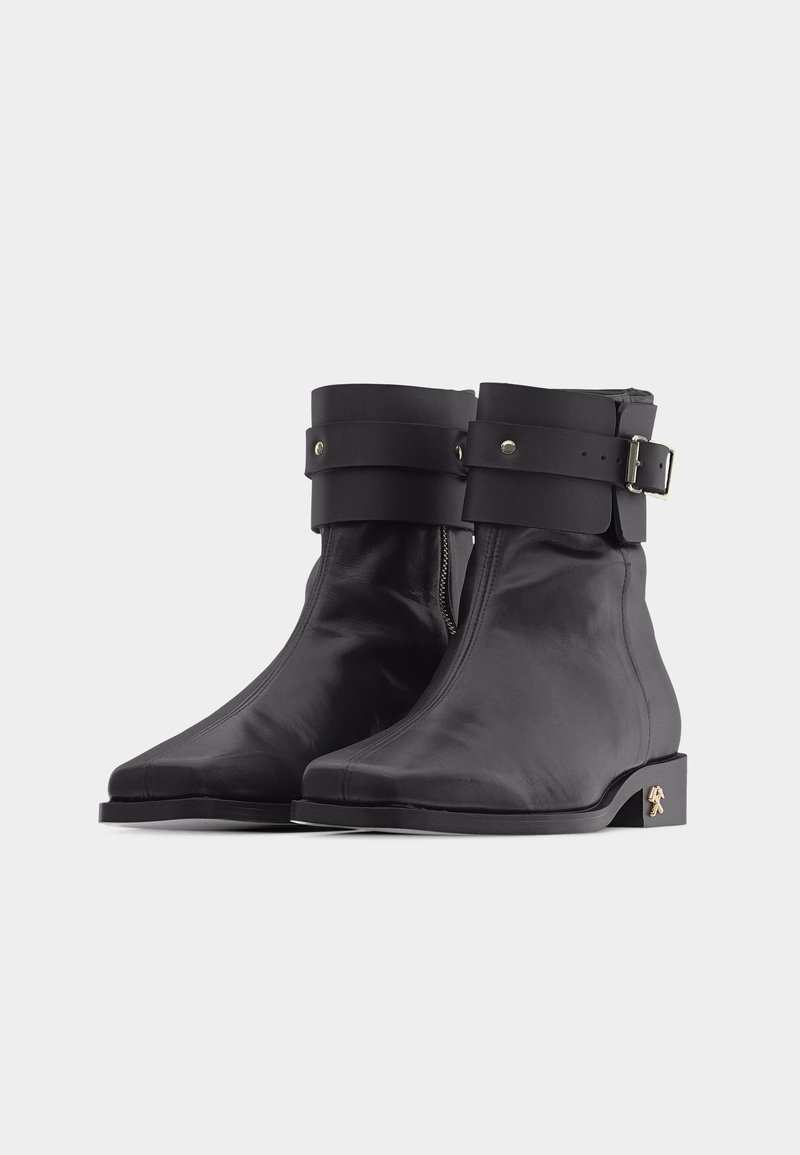 Coppia di stivaletti alla caviglia in pelle nera con cerniera laterale, ampia fibbia con cinturino sulla parte superiore e piccolo emblema metallico sul tallone.