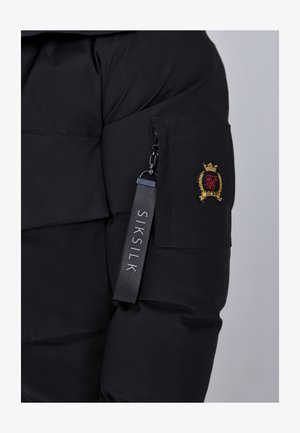 Mustapuffatakki, jossa on vetoketjullinen tasku, brodeeratun logon ja "SIKSILK" -kangastagin kanssa. Raskas tekstuurinen ulkomateriaali.