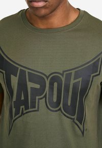 Olivgrünes Baumwoll-T-Shirt mit großem schwarzem "TAPOUT"-Logo. Das Shirt hat einen Rundhalsausschnitt und kurze Ärmel mit glatter Textur.